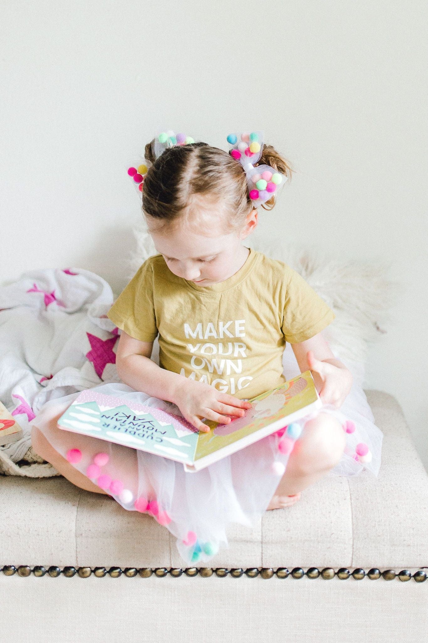 tutu joli pom pom tutu skirt in white for kids with bow hairtie and poms, a child reading Allison in wonderland book, pom pom hair tie bow for children, designer hair ties, designer kids accessories, tutu joli white pom pom tutu skirt, pom pom tutu, white tutu skirt for toddlers, pom pom hair bow, pom pom bow ponytail holder, pom pom hair accessories, birthday tutu white, rainbow pom pom balls tutu, tootoo, pompoms